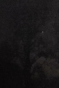Ein überwiegend dunkles und körniges Bild mit einem einzelnen kleinen hellen Fleck oben rechts, möglicherweise einem entfernten Licht oder Stern, und schwachen, undeutlichen Formen im Hintergrund.