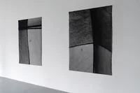 An einer weißen Galeriewand sind zwei große abstrakte Textilkunstwerke in Schwarzweiß ausgestellt. Jedes weist sich kreuzende Linien und strukturierte Muster mit einer kleinen sternförmigen Form im unteren Bereich auf.