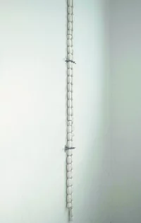 Eine vertikale Reihe weißer, ovaler Objekte, die an einer schlichten weißen Wand angebracht und von zwei sichtbaren Metallklammern an ihrem Platz gehalten werden.